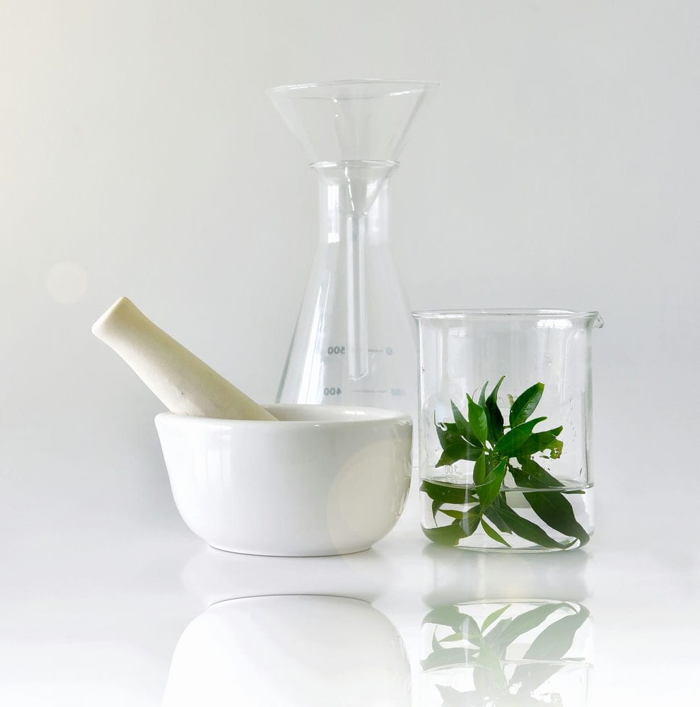 Mortar and pestle beside laboratory beakers holding green botanicals