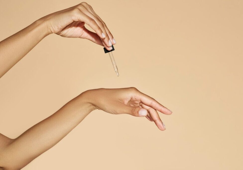 Hand using a dropper to apply a skincare serum onto another outstretched hand